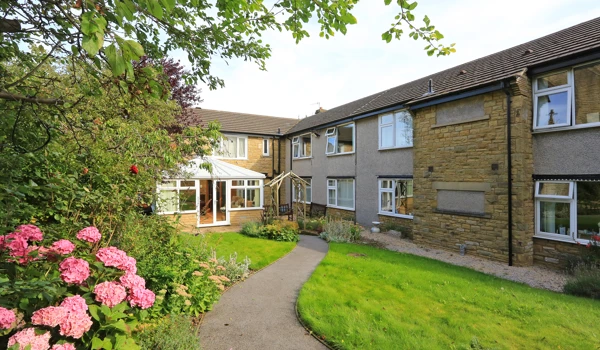 A path leading to the front of the house through flowers and trees